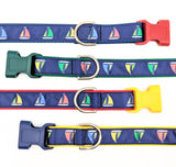 Four sailboat dog collars shown horizontally with different colors of nylon webbing and plastic buckles. All collars are navy blue ribbon with sailboat designs in red, yellow, green, and blue. Plastic buckles in red, green, yellow, and navy blue are shown.