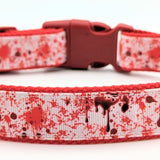 Dog collar with blood splatter design. Collar has a red nylon on the underside with white ribbon with red blood splatter design, and the plastic hardware is red in color.