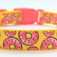Dog collar with yellow background with pink frosted donuts with sprinkles on it. Collar has a neon pink buckle closure.
