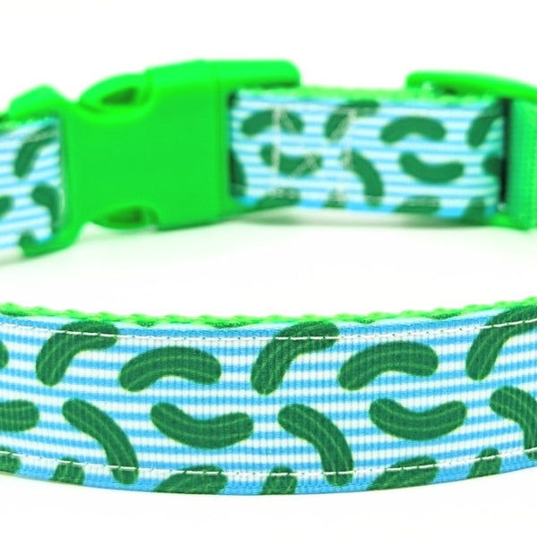 zoomed in image of dog collar with green pickles and blue and white stripes. Collar has lime green webbing behind the striped pickle ribbon and has a lime green buckle.