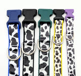 A lineup of handmade Holy Cow! cow print dog collars in sizes XS, Small, Medium, and Large, showing the black and white bovine pattern on shimmering satin ribbon with durable nylon backing.