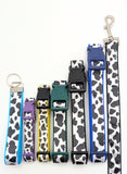 A lineup of handmade Holy Cow! cow print dog collars in sizes XS, Small, Medium, and Large, and a leash, all showing the black and white bovine pattern on shimmering satin ribbon with durable nylon backing.