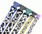 A lineup of handmade Holy Cow! cow print dog collars in sizes XS, Small, Medium, and Large, showing the black and white bovine pattern on shimmering satin ribbon with durable nylon backing.