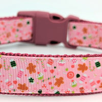 Pink Christmas dog collar made with pink ribbon with various Christmas candies on it, including gingerbread, candy cane, cupcakes, and other candies. Collar has raspberry pink nylon on the underside and a raspberry pink buckle. All shown against a plain white background.