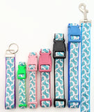 A row of dog collars with seafoam green cartoon dinosaur patterns displayed in various sizes and colors