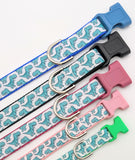 A row of dog collars with seafoam green cartoon dinosaur patterns displayed in various sizes and colors
