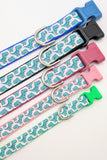 A row of dog collars with seafoam green cartoon dinosaur patterns displayed in various sizes and colors