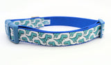 Dog collar featuring seafoam green cartoon T-Rex dinosaurs on a white ribbon, sewn onto royal blue nylon webbing and with a blue side-release buckle.