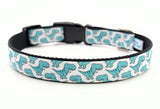 Dog collar featuring seafoam green cartoon T-Rex dinosaurs on a white ribbon, sewn onto black nylon webbing and with a black side-release buckle.
