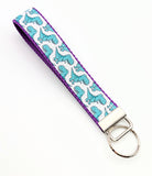 Key fob featuring seafoam green cartoon T-Rex dinosaurs on a white ribbon, sewn onto purple nylon webbing.