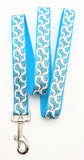 Dog leash featuring seafoam green cartoon T-Rex dinosaurs on a white ribbon, sewn onto turquoise nylon webbing.