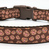 a zoomed in image of the Medium sized dog collar with brown candy cookie design on it. The collar has brown nylon on the underside and a brown plastic buckle.