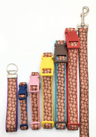 Side by side view of key fob and dog collars and a leash in different sizes in a brown candy cookie design.  Each collar, leash, and key fob are made with different colored nylon & buckles.