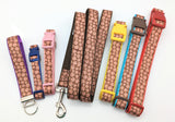 Several brown candy cookie patterned items laid side by side. Including a key fob, an XS dog collar, a Small dog collar, a leash, a Medium dog collar, a Large dog collar, and an XL sized collar.