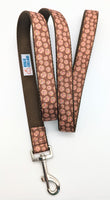 A brown candy cookie patterned dog leash with brown nylon on the underside, a silver metal leash attachment, and a white label with the Rogue Collars logo on it.