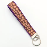 A brown candy cookie pattern key fob with purple nylon on the underside, with a silver metal clasp and key ring.